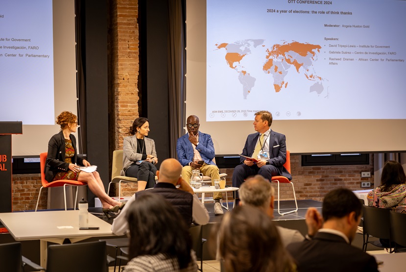 Four speakers sit on the stage, behind them is a map showing where elections will be held in 2024, in the foreground are some audience members.